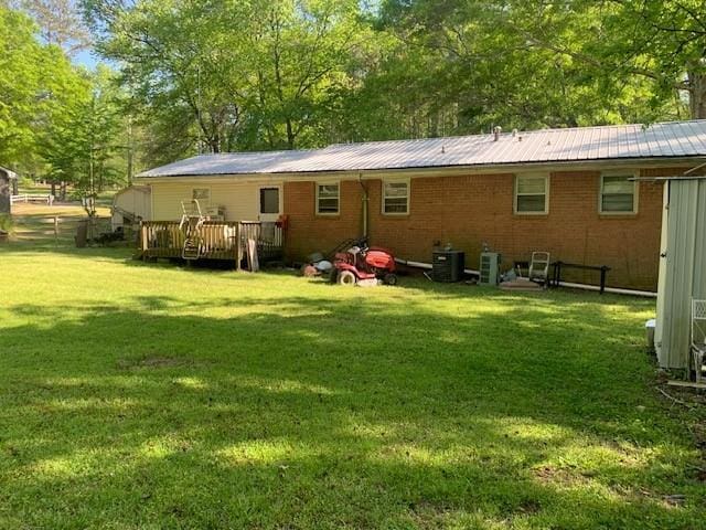 back of property featuring a deck, brick siding, metal roof, central AC, and a lawn