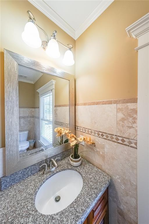 3416 Harrison Rd, Atlanta, GA 30344 - bathroom with tile walls, ornamental molding, toilet, vanity, and a wainscoted wall