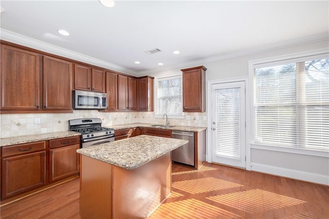 kitchen with appliances with stainless steel finishes, plenty of natural light, light wood-type flooring, a kitchen island, and ornamental molding