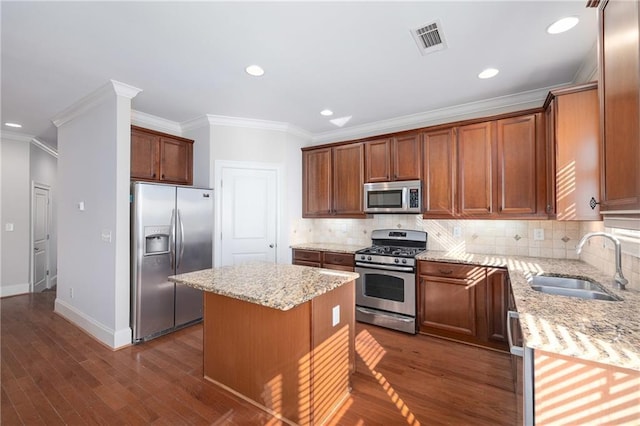kitchen featuring light stone countertops, appliances with stainless steel finishes, ornamental molding, sink, and a kitchen island