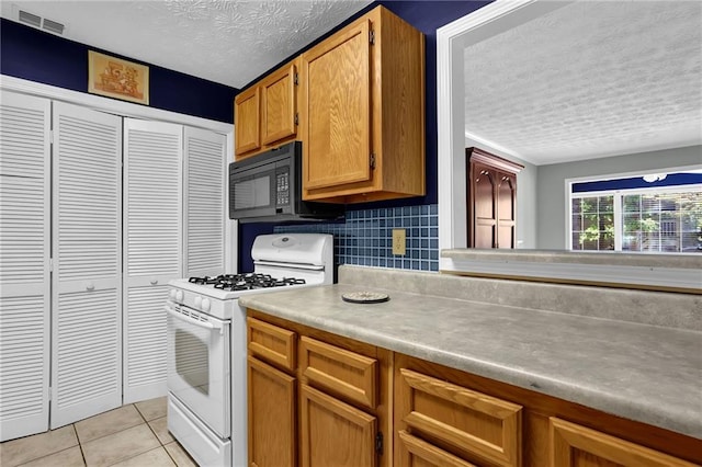 kitchen featuring white range with gas stovetop, backsplash, a textured ceiling, and light tile patterned floors