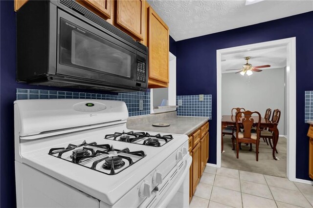 kitchen with light tile patterned floors, ceiling fan, a textured ceiling, white gas range, and decorative backsplash