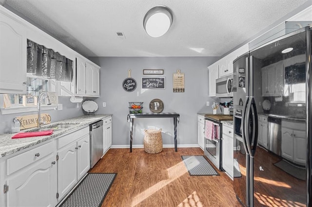 kitchen with hardwood / wood-style flooring, stainless steel appliances, white cabinetry, and sink