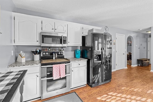 kitchen featuring a textured ceiling, appliances with stainless steel finishes, white cabinetry, and light wood-type flooring