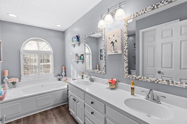 bathroom with a textured ceiling, wood-type flooring, vanity, toilet, and a bathing tub