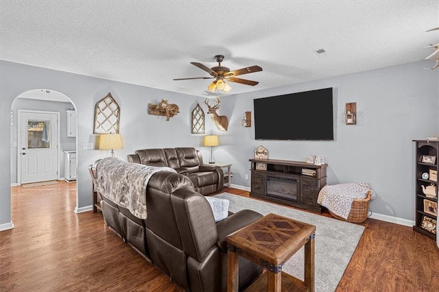 living room with ceiling fan, dark wood-type flooring, a textured ceiling, and a fireplace