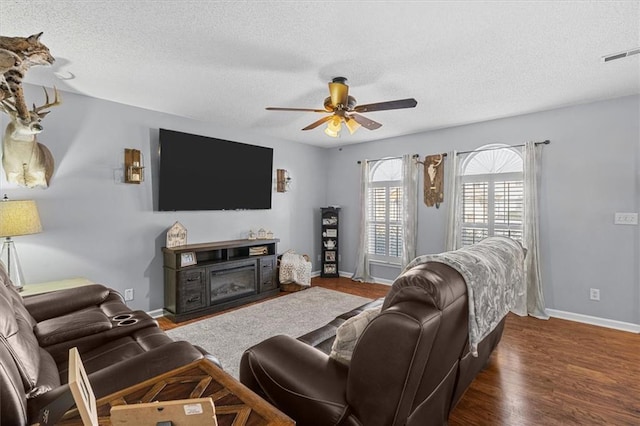 living room featuring ceiling fan, dark hardwood / wood-style flooring, a fireplace, and a textured ceiling