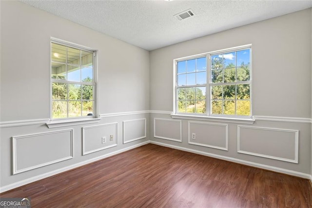 unfurnished room featuring dark wood-style floors, a textured ceiling, wainscoting, and visible vents