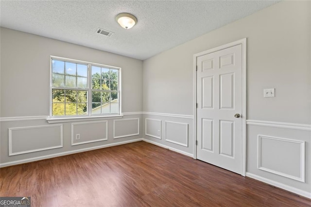 unfurnished room featuring dark wood-style flooring, visible vents, a decorative wall, and a textured ceiling