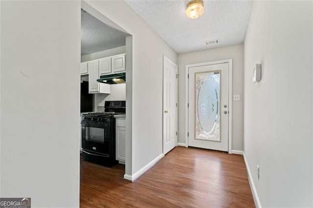 foyer entrance with baseboards, a textured ceiling, visible vents, and wood finished floors