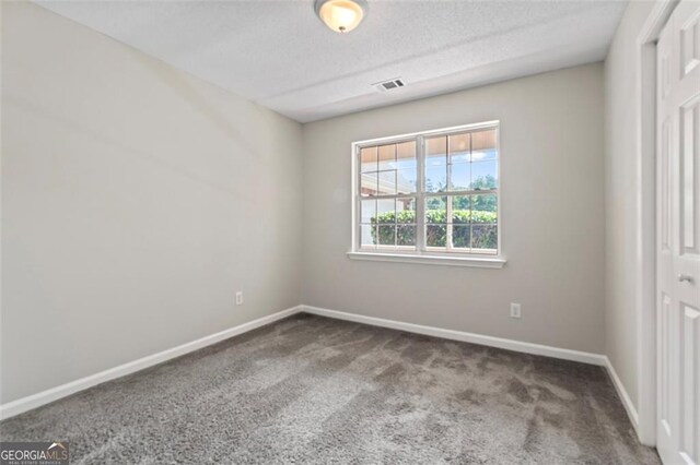 unfurnished room featuring visible vents, dark carpet, a textured ceiling, and baseboards