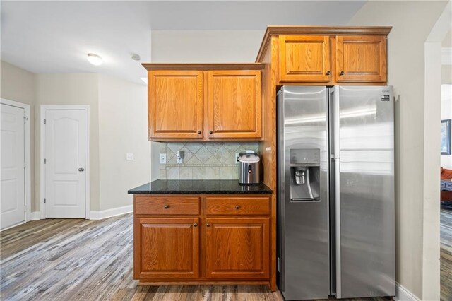 kitchen featuring backsplash, dark stone countertops, stainless steel refrigerator with ice dispenser, and hardwood / wood-style flooring