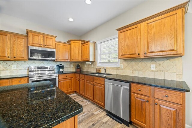 kitchen with dark stone counters, sink, decorative backsplash, appliances with stainless steel finishes, and light hardwood / wood-style floors