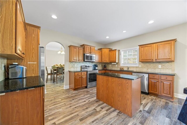 kitchen with appliances with stainless steel finishes, dark stone counters, sink, hardwood / wood-style floors, and a kitchen island