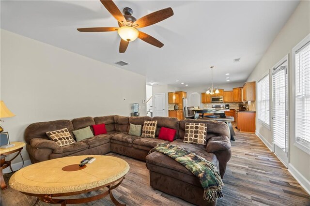 living room featuring ceiling fan with notable chandelier and light hardwood / wood-style floors