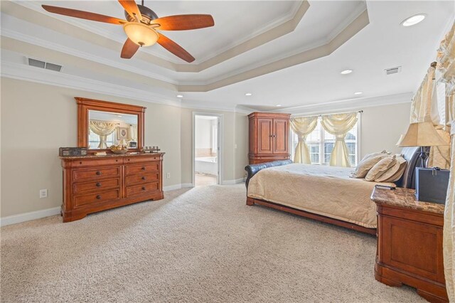 carpeted bedroom with a tray ceiling, connected bathroom, ceiling fan, and ornamental molding