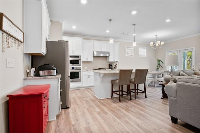 kitchen featuring appliances with stainless steel finishes, white cabinetry, light hardwood / wood-style flooring, ornamental molding, and pendant lighting