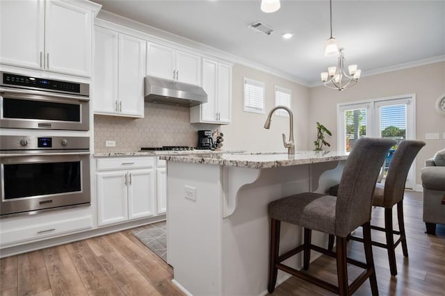 kitchen with light hardwood / wood-style flooring, an island with sink, and stainless steel double oven