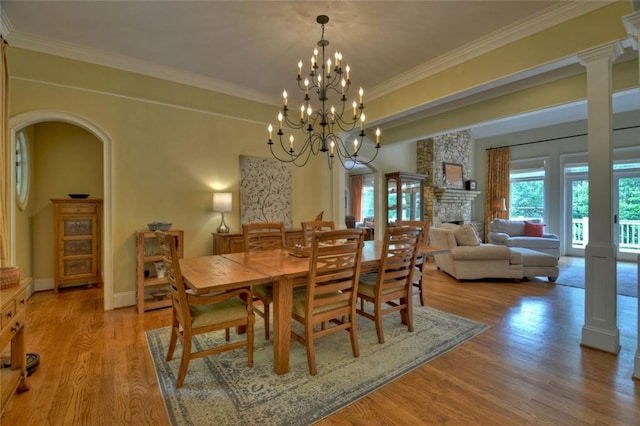 dining room with a stone fireplace, ornamental molding, ornate columns, and light wood-type flooring