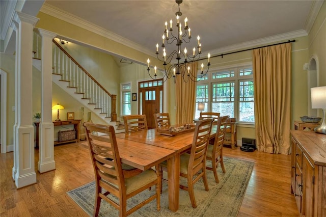 dining area featuring an inviting chandelier, crown molding, decorative columns, and light hardwood / wood-style floors