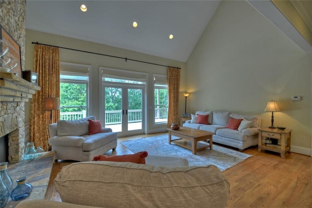 living room featuring light hardwood / wood-style floors, a stone fireplace, high vaulted ceiling, and french doors