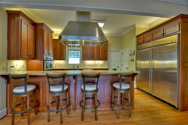 kitchen with tasteful backsplash, island range hood, stainless steel appliances, and a kitchen bar