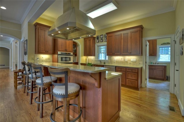 kitchen featuring island range hood, a breakfast bar area, kitchen peninsula, stainless steel appliances, and light stone countertops