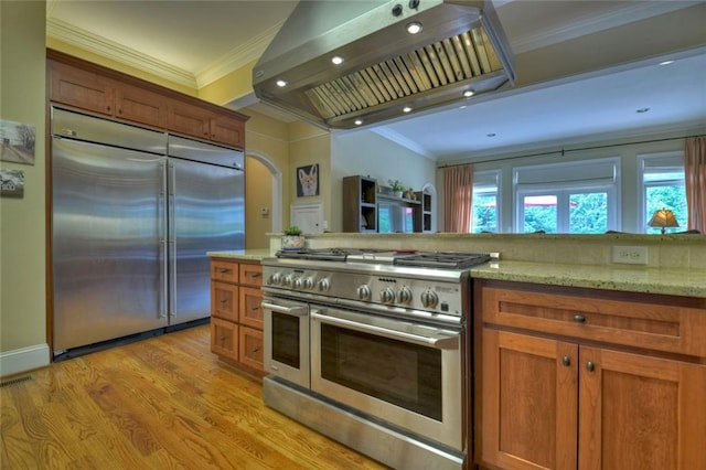 kitchen with crown molding, light stone counters, premium appliances, exhaust hood, and light wood-type flooring