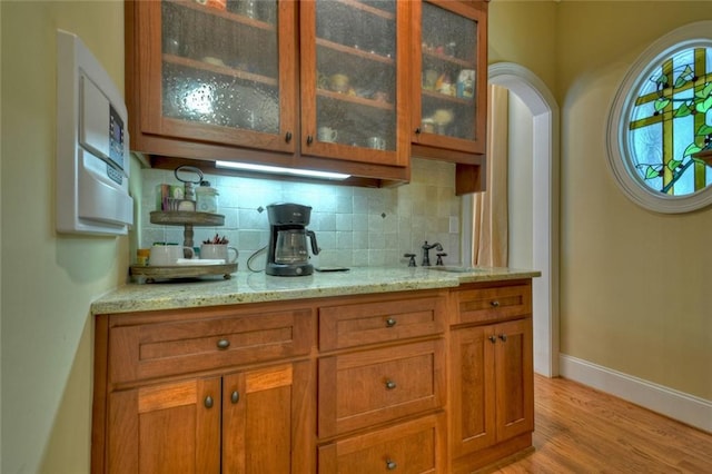 bar featuring tasteful backsplash, sink, light hardwood / wood-style flooring, and light stone countertops