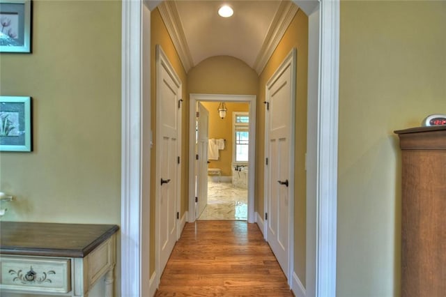 hallway with vaulted ceiling, crown molding, and light wood-type flooring