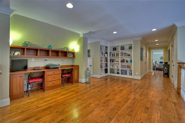 office space featuring built in features, built in desk, ornamental molding, and light wood-type flooring