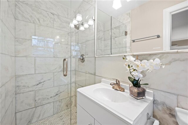 bathroom featuring a shower with door, vanity, and tile walls