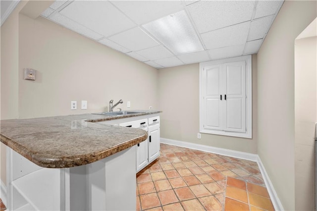 kitchen featuring sink, light tile patterned floors, a paneled ceiling, white cabinets, and kitchen peninsula