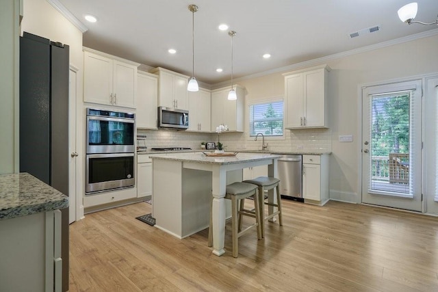 kitchen featuring visible vents, a sink, decorative backsplash, stainless steel appliances, and crown molding