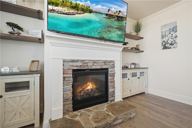 interior details with a stone fireplace, wood finished floors, baseboards, and ornamental molding