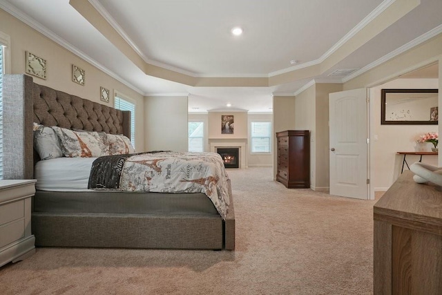 bedroom featuring a tray ceiling, light carpet, a lit fireplace, and ornamental molding