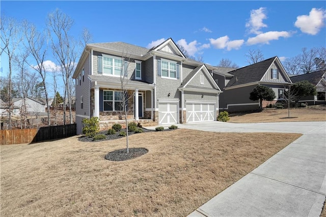 view of front of home with driveway, stone siding, fence, a front yard, and a garage