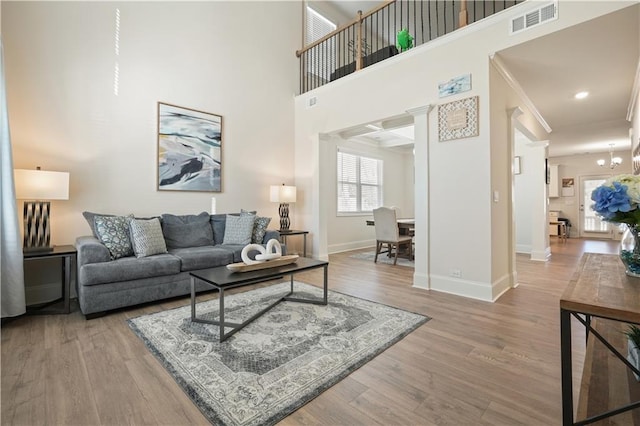 living area featuring visible vents, baseboards, ornamental molding, a high ceiling, and wood finished floors