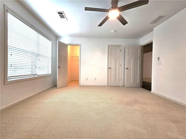 unfurnished bedroom with a closet, ceiling fan, light carpet, and a walk in closet