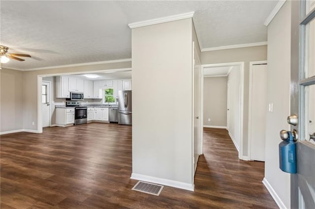 interior space featuring white cabinets, appliances with stainless steel finishes, dark wood-type flooring, and ornamental molding