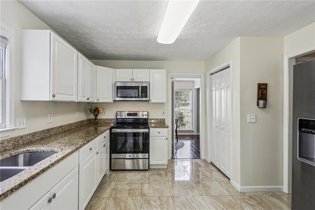 kitchen with a textured ceiling, light stone counters, marble finish floor, stainless steel appliances, and white cabinetry