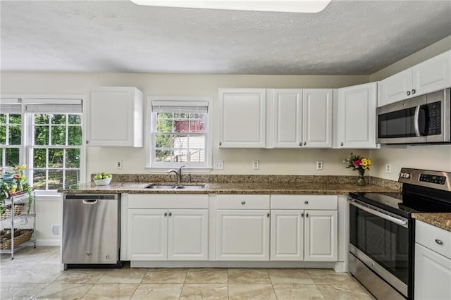 kitchen with a textured ceiling, a sink, white cabinets, dark stone countertops, and stainless steel appliances