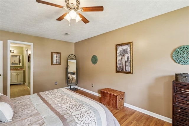 bedroom with a ceiling fan, visible vents, wood finished floors, baseboards, and ensuite bath