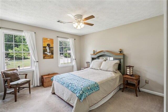 bedroom featuring visible vents, baseboards, ceiling fan, light colored carpet, and a textured ceiling