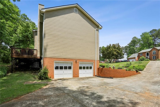 view of property exterior featuring an attached garage, brick siding, a deck, a chimney, and concrete driveway