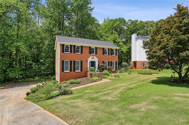colonial house with a chimney, concrete driveway, a front lawn, and brick siding