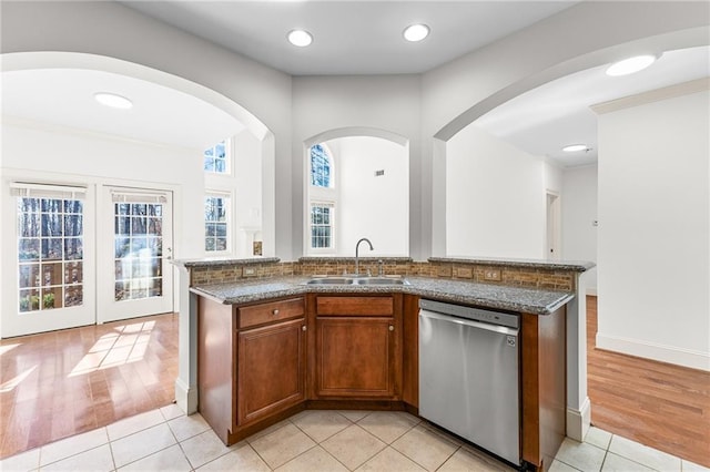 kitchen featuring dark stone counters, brown cabinetry, dishwasher, a sink, and light tile patterned flooring