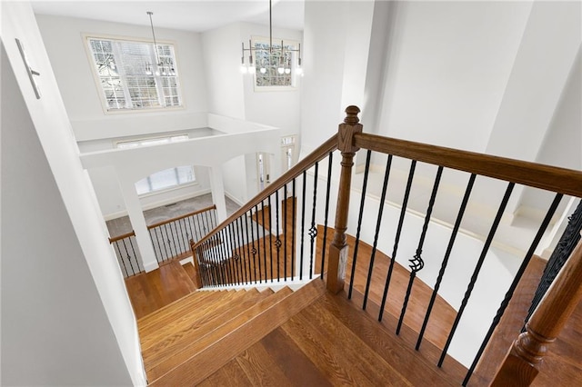 stairway featuring wood finished floors, a towering ceiling, and an inviting chandelier