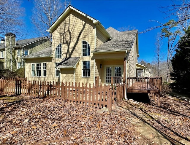 rear view of house with a deck, french doors, a fenced front yard, and a shingled roof