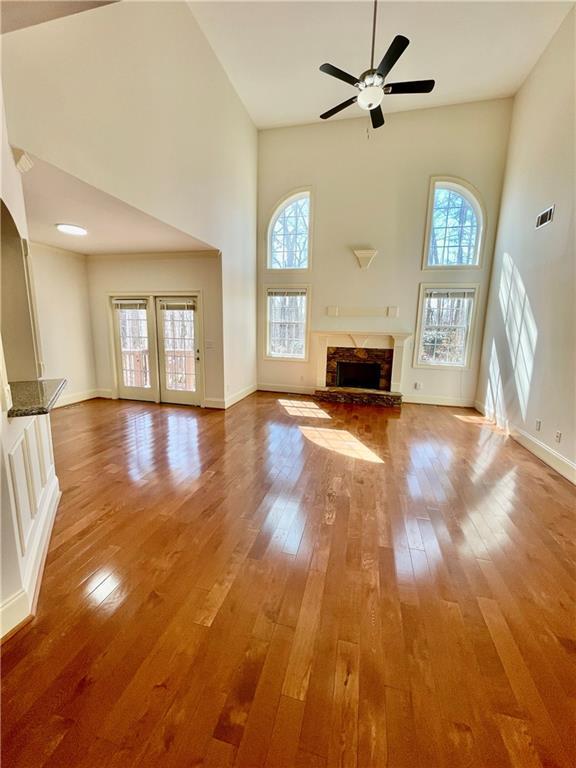 unfurnished living room with ceiling fan, a high ceiling, a fireplace, baseboards, and wood-type flooring